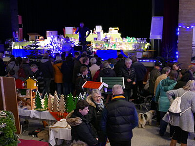 Weihnachtsbasar der Rotenburger Werke in einem weihnachtlich geschmückten Saal mit vielen Besuchern, auf einer Bühne aufgereihte und stimmungsvoll angeleuchtete Preise einer Tombola