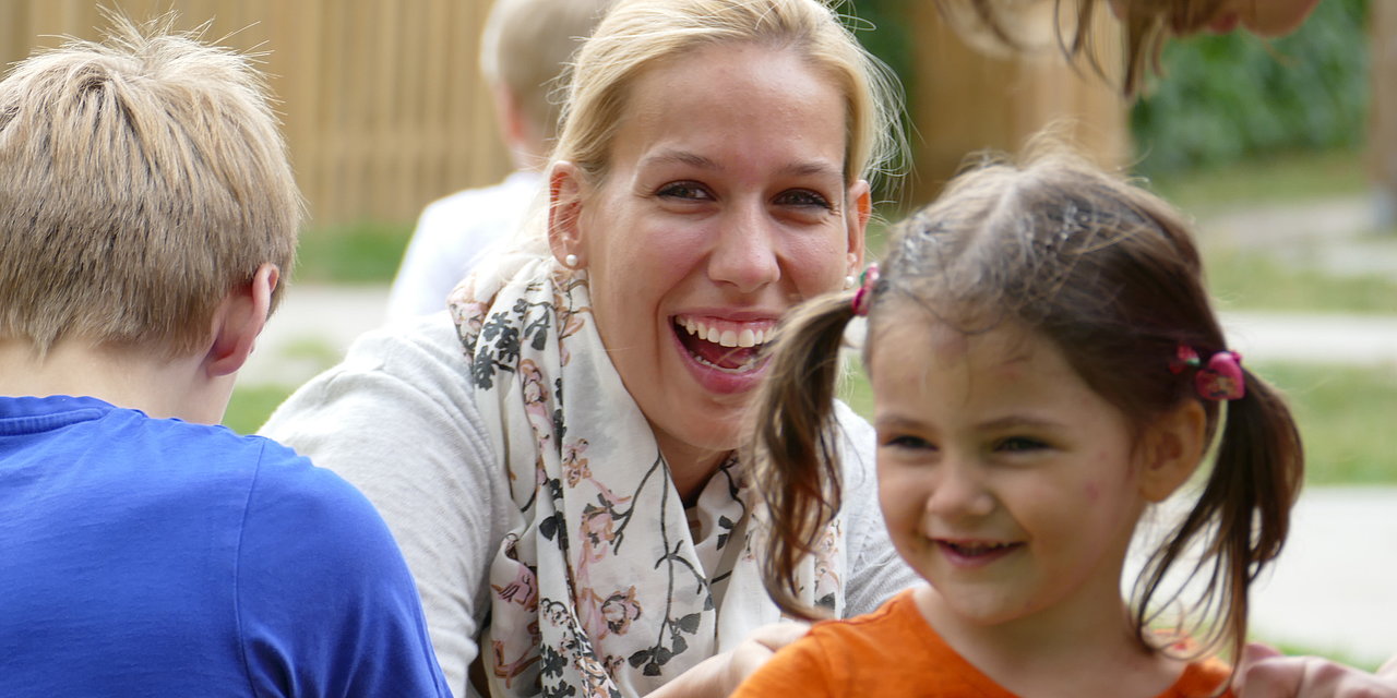 Eine lachende Mitarbeiterin ist von Kindern umgeben