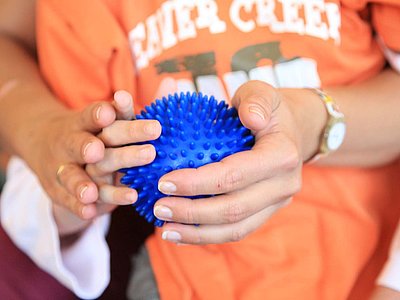 Zwei kindliche Hände umfassen einen Igel-Ball, die Hand einer Erwachsenen berührt die Hände.
