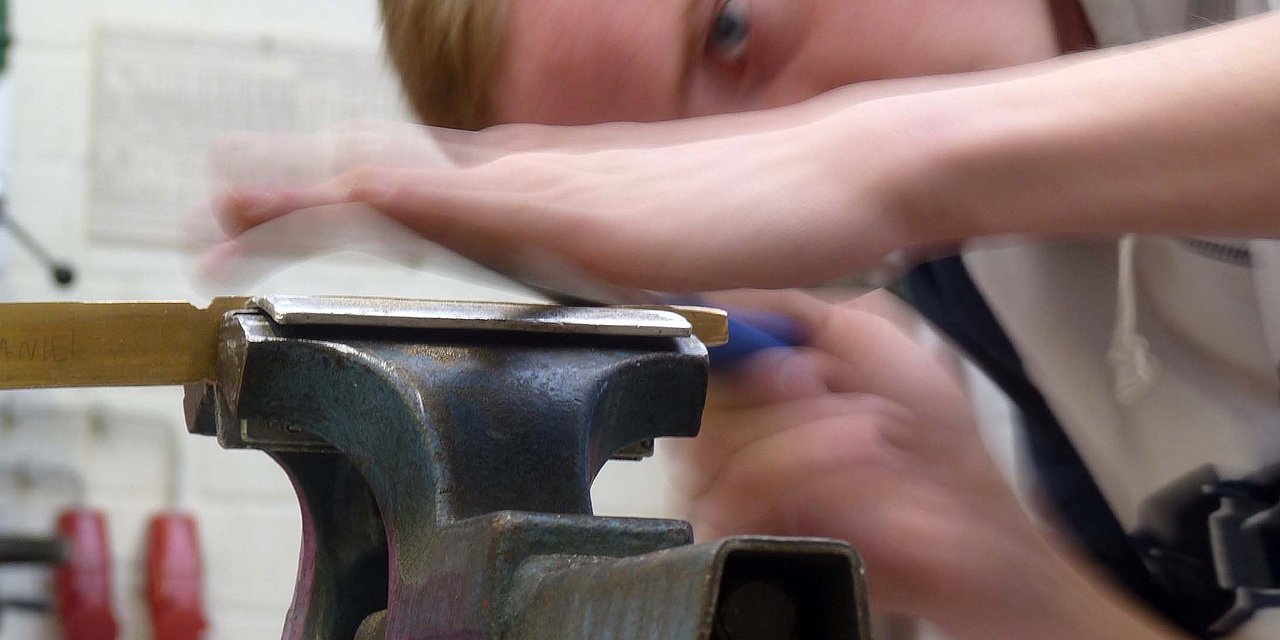 Ein junger mit konzentriertem Blick schleift Metall auf einer Werkbank