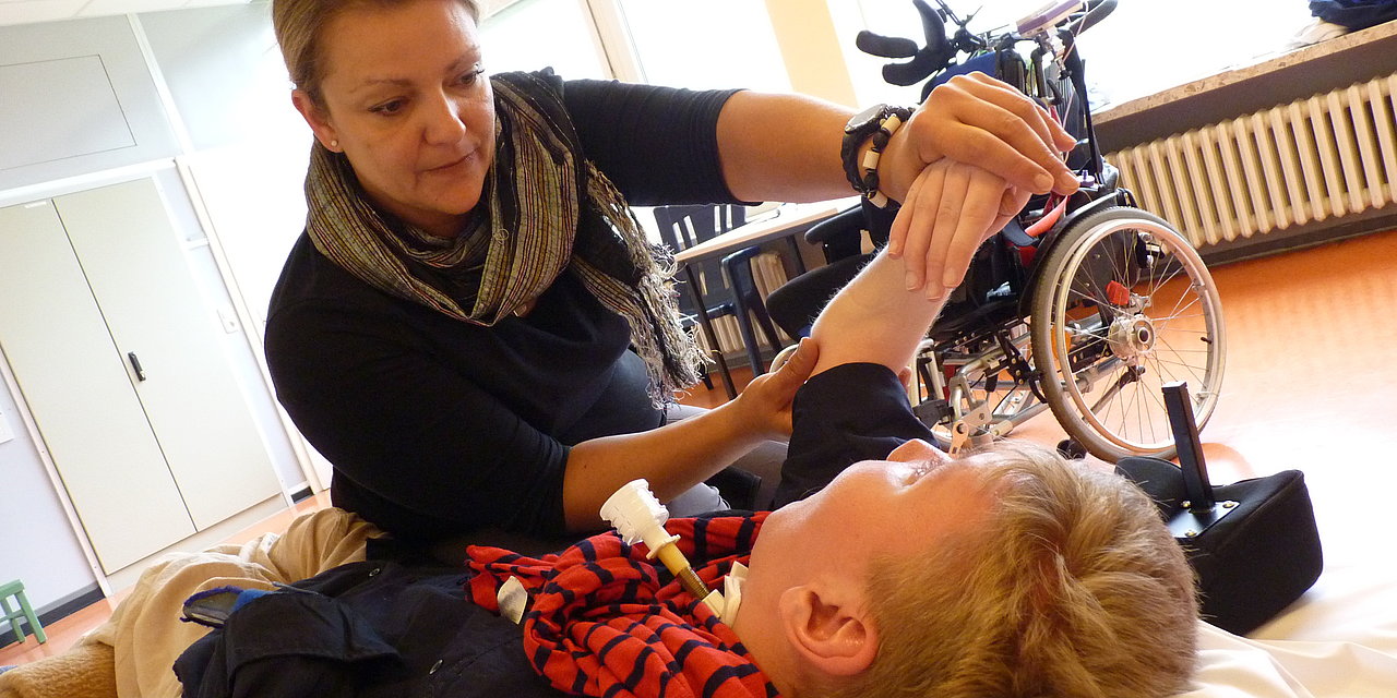 Eine Physiotherapeutin führt mit konzentriertem Lächeln die Hände einer Patientin