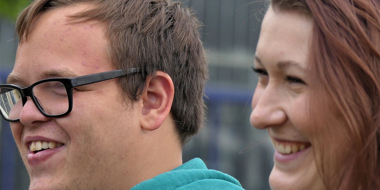 Ein junger Mann und eine junge Mitarbeiterin blicken lächelnd in eine Richtung