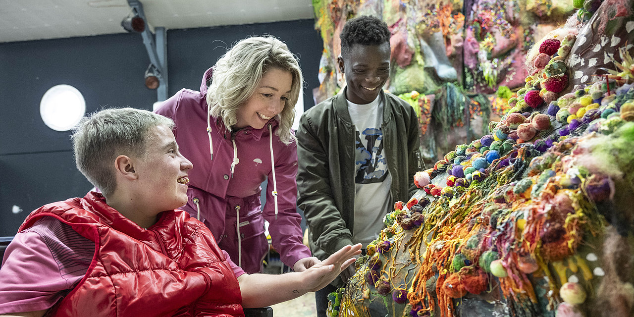 Vier junge Menschen betrachten ein buntes Kunstwerk in einem Atelier