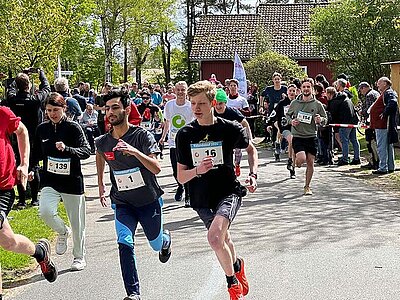 Eine Gruppe junger, gut gelaunter Menschen sitzt im Freien nebeneinander 