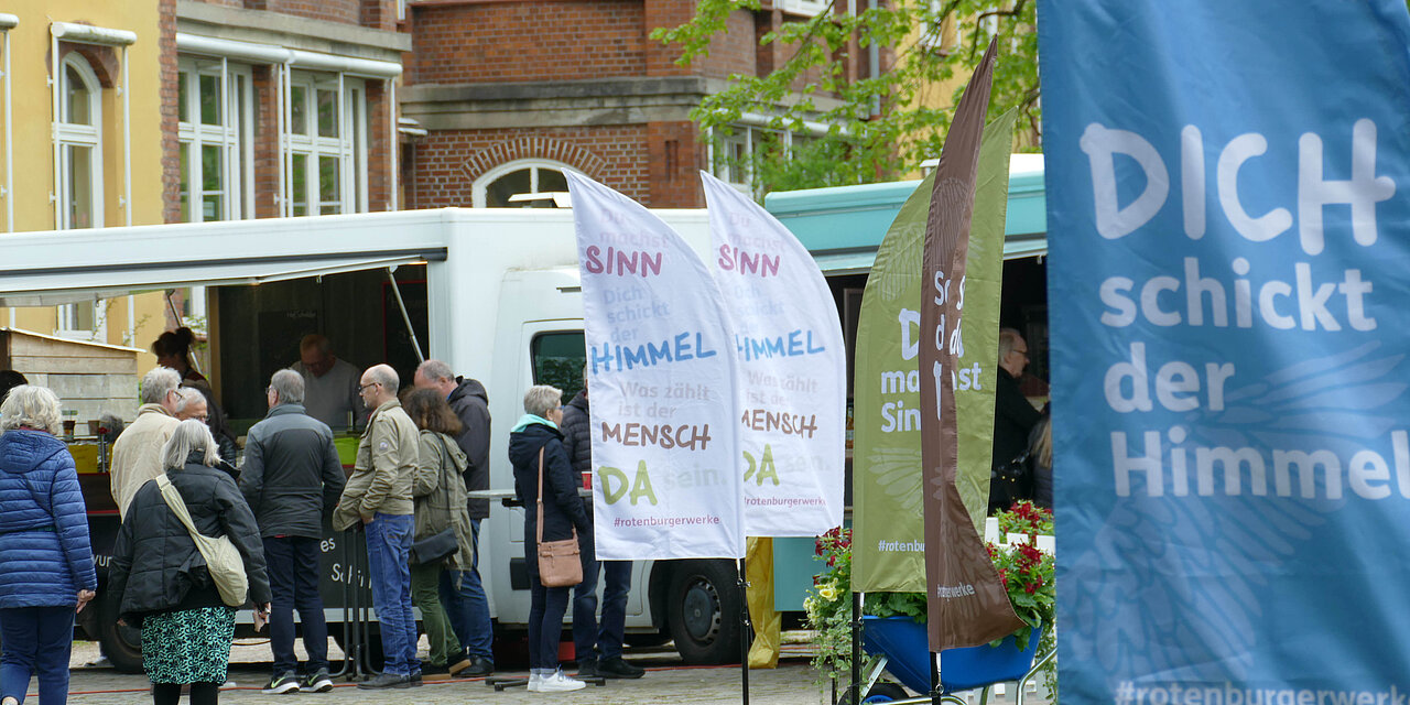Junge Leute stehen auf einer Wiese in Gruppen zusammen, Fahnen mit Dich schickt der Himmel und anderen Slogans sind zu lesen