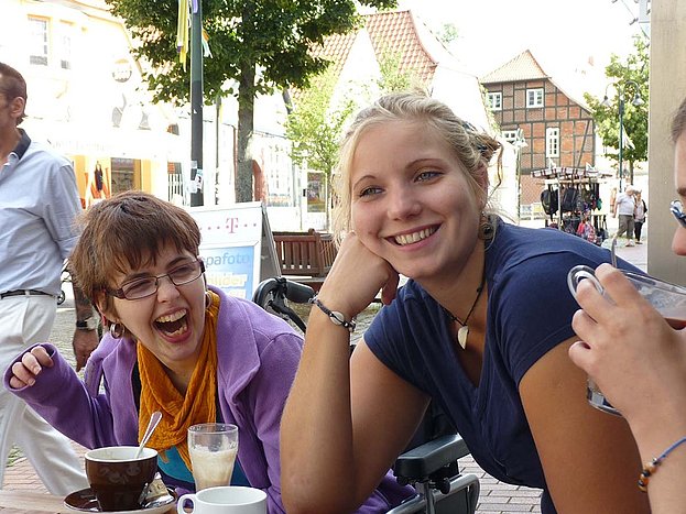 Junge Frauen sitzen in einem Eis-Café vor ihrem Heißgetränk und lachen