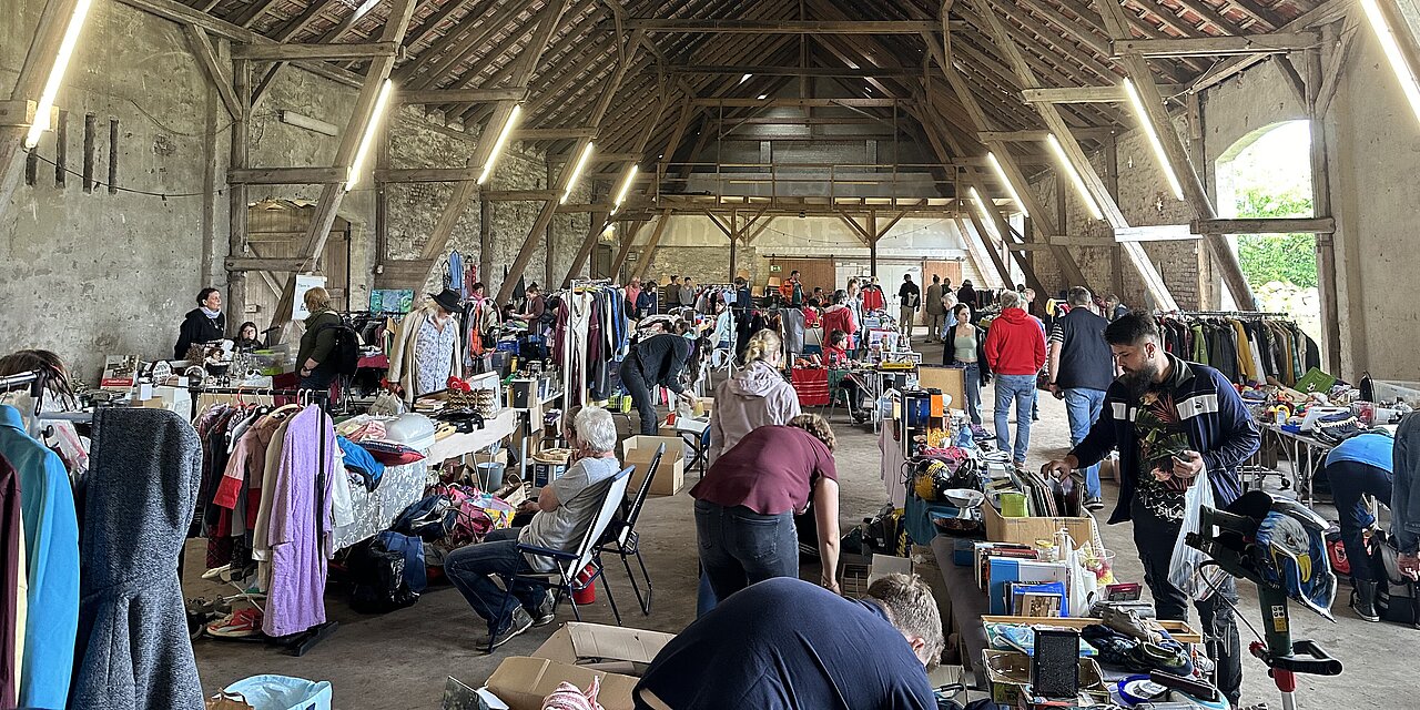 Eine große Scheune von innen, Menschen schlendern von einem Stand des Hökermarktes zum nächsten