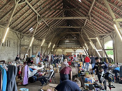 Eine große Scheune von innen, Menschen schlendern von einem Stand des Hökermarktes zum nächsten