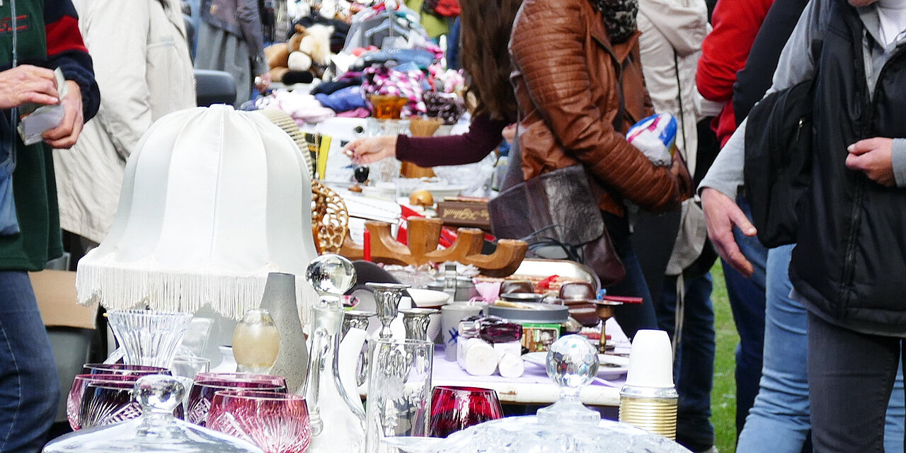 Ein langer Tisch mit Geschirr und Trödel, an dem Menschen vorübergehen 