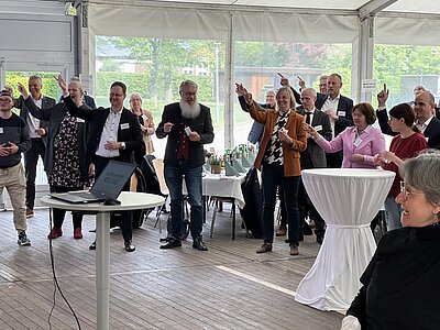 Gäste beim Jahresempfang stehen im Veranstaltungszelt beieinander und blicken fröhlich in Richtung einer Bühne und bewegen ihre Arme
